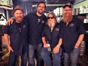 Four friends wear matching shirts in a brewery taproom